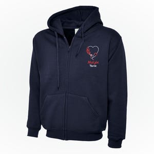 Può includere: Felpa con cappuccio blu navy con cerniera e tasche anteriori. Sul petto sinistro è presente un disegno a forma di cuore con uno stetoscopio e accenti floreali, insieme al nome "Malzie" e alla parola "Nurse" in rosso.