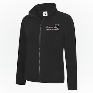 Könnte beinhalten: Schwarze Fleece-Jacke mit Reißverschluss und hohem Kragen. Die Jacke trägt den Namen "Jemma" und eine Zahngrafik sowie die Worte "Dental Hygienist" in einer Schreibschrift. Die Jacke hat einen durchgehenden Reißverschluss und zwei Seitentaschen.
