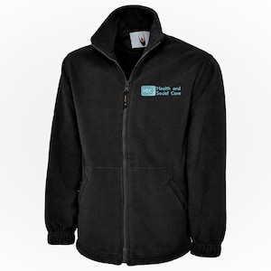 Könnte beinhalten: Schwarze Fleecejacke mit durchgehendem Reißverschluss, hohem Kragen und zwei Vordertaschen. Der Text "Health and Social Care" ist in Hellblau auf der linken Brust aufgedruckt. Mit gerippten Bündchen und Saum.