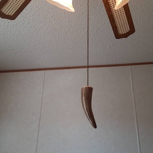 May include: A ceiling fan with four wooden blades and a decorative antler pull. The blades have a woven cane pattern. The antler pull hangs from a beaded chain.