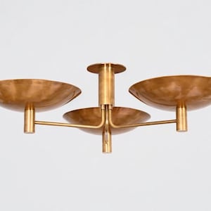 May include: A brass ceiling light fitting featuring three wide, shallow, bowl-shaped shades attached to a central vertical stem. The metal has a brushed, warm-toned finish, and the design includes horizontal arms extending from the centre.