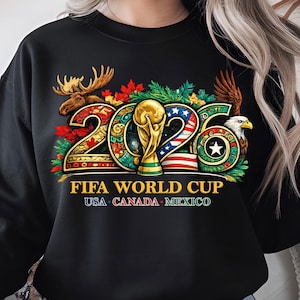 May include: Black sweatshirt featuring a colorful design for the 2026 FIFA World Cup. The design includes the text "2026 FIFA WORLD CUP USA CANADA MEXICO" with a trophy, moose, and eagle.