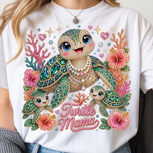 May include: White t-shirt featuring a bejeweled turtle family design. The design includes a large turtle with a pearl necklace, two smaller turtles, coral, and hibiscus flowers. The text "Turtle Mama" is written in pink script.