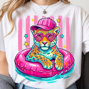 Op de afbeelding: Wit T-shirt met een kleurrijke luipaard die een hartvormige zonnebril en een roze pet draagt, drijvend in een roze zwemband. Het ontwerp bevat roze en witte strepen en steraccenten, wat een leuke, zomerse sfeer creëert.