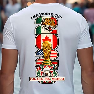 May include: White t-shirt featuring a colorful graphic for the FIFA World Cup 2026. The design includes a jaguar, the Canadian flag, the World Cup trophy, the American flag, a soccer ball, and the text "CANADA USA MEXICO".