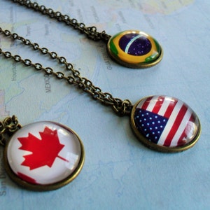 May include: Three necklaces with round glass pendants featuring the flags of Canada, the United States, and Brazil. The pendants are attached to bronze chains.