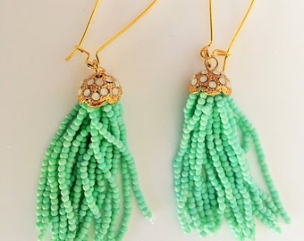 May include: A pair of gold dangle earrings with green beaded tassels. The tassels are made of small, round beads and are about 2 inches long.