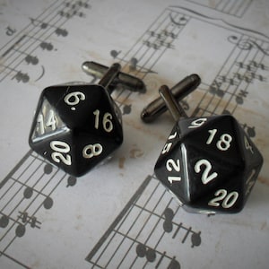 May include: Two black cufflinks shaped like twenty-sided dice with white numbers.