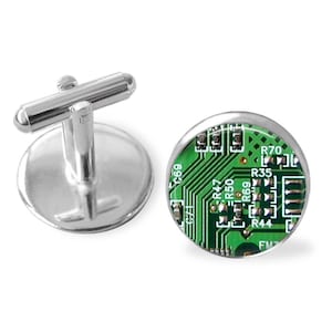 May include: A pair of silver cufflinks featuring a green circuit board design. The cufflinks are round and have a silver metal frame.