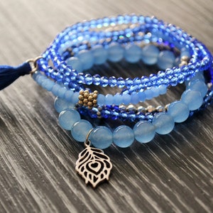 May include: A blue and silver beaded bracelet with a blue tassel and a silver feather charm.