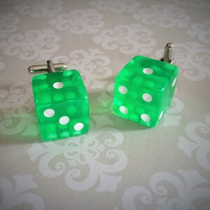 May include: A pair of green dice cufflinks with white dots. The dice are made of clear plastic and have a shiny finish.
