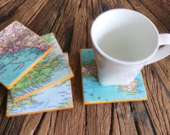 May include: Set of four square coasters featuring vintage map designs. The coasters are made of cork and have a yellow border. A white mug is sitting on one of the coasters.