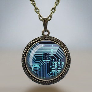 May include: A circular pendant necklace featuring a circuit board design. The pendant has a bronze-coloured frame and chain. The circuit board design is in shades of blue and black, with intricate lines and details.