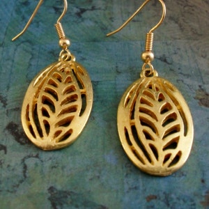 May include: A pair of gold-colored earrings. Each earring features an oval-shaped design with a cutout leaf pattern. The earrings have a hook closure for easy wear. The earrings are a bright gold color.