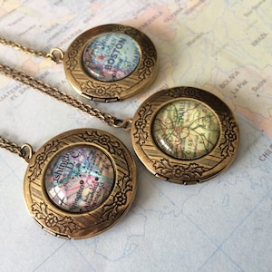 May include: Three gold locket necklaces with map designs inside. The lockets feature a floral design around the edges. The maps inside the lockets are of Boston, Paris, and Washington D.C.