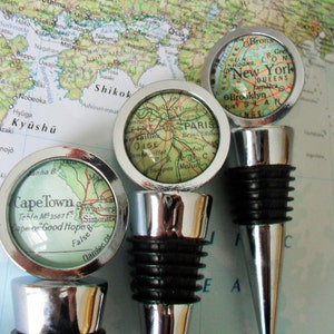 May include: Three silver bottle stoppers featuring maps of Cape Town, Paris, and New York City. Each stopper has a black rubber base.