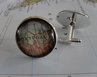 May include: A pair of silver cufflinks with a map of Portugal in the center. The map is in a glass dome and the cufflinks are on a white background.