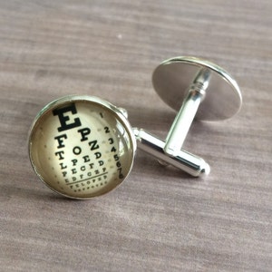 以下が含まれることがあります： 丸いガラス製のカボションが付いた銀製のカフスボタン。ヴィンテージの視力検査表には、E、F、P、Z、T、O、L、P、E、D、P、E、C、D、F、E、D、C、Z、P、E、L、O、P、E、D、F、O、Tの文字と1から7までの数字が書かれています。