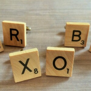 May include: Set of six wooden cufflinks, each featuring a letter tile from the game Scrabble. The letters spell out "C.R.O.X.L.B."