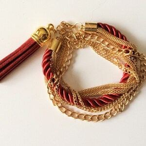 May include: A multi-strand bracelet with a red tassel. The bracelet is made of gold chains and red cord.