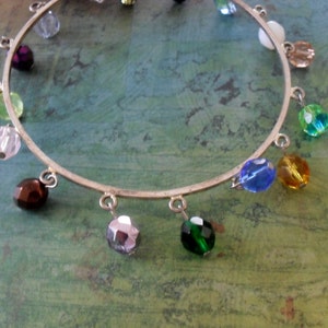 May include: A silver bangle bracelet with a variety of colored glass beads, including green, blue, purple, brown, and white.