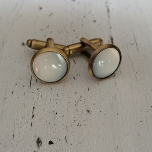 May include: A pair of gold cufflinks with white round inlays.