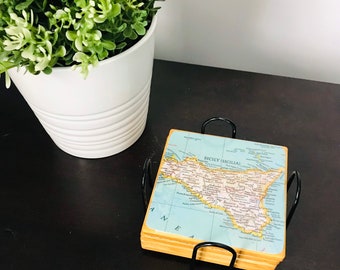 May include: A set of four coasters featuring a map of Sicily, Italy. The coasters are made of wood and have a black metal holder.