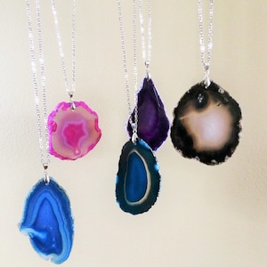 May include: Five agate slice necklaces with silver chains. The agate slices are in shades of pink, purple, blue, and brown.