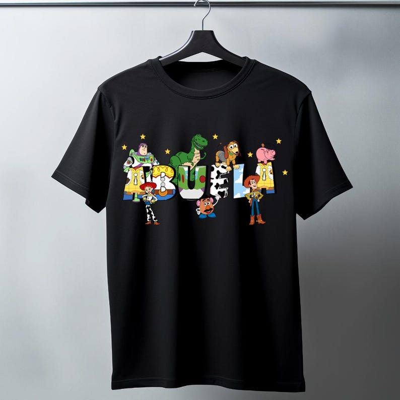 May include: Black t-shirt featuring the word "BUEL" in colorful letters, each letter designed with characters from the animated film Toy Story. The shirt includes images of Buzz Lightyear, Rex, Woody, and other characters.
