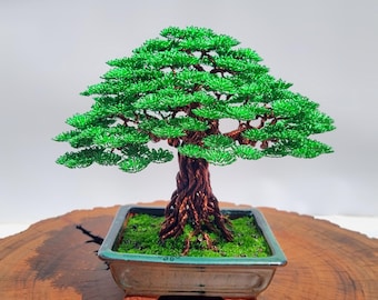Puede incluir: Escultura de árbol bonsái hecha a mano. El árbol presenta una estructura de alambre detallada con hojas verdes y un tronco marrón. Está plantado en una maceta cuadrada de cerámica llena de musgo verde. El bonsái se exhibe sobre una superficie de madera.