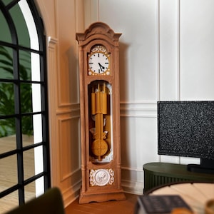 Könnte beinhalten: Eine hohe Standuhr aus hellbraunem Holz mit einem weißen Zifferblatt und schwarzen Zeigern, einem zentralen Pendelmechanismus mit goldfarbenen Gewichten sowie dekorativen weißen Reliefschnitzereien am oberen und unteren Ende des Rahmens.