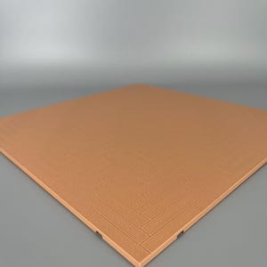Op de afbeelding: Een vierkante, lichtbruine tegel met een verhoogd, in reliëf aangebracht visgraatpatroon over het gehele oppervlak. De tegel heeft een egale kleur en een geometrische textuur die het uiterlijk nabootst van kleine, rechthoekige houten planken in een klassieke V-vormige indeling.