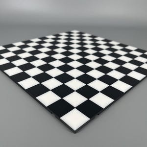 Op de afbeelding: Een vierkant schaakbord met een klassiek afwisselend patroon van zwarte en witte vierkanten. Het bord is plat met een gladde, schone afwerking en toont een standaard rasterindeling die wordt gebruikt voor het schaakspel, vanuit een hoek.