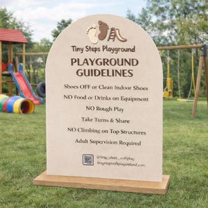 以下が含まれることがあります： 「Tiny Steps Playground PLAYGROUND GUIDELINES」と書かれた、茶色の文字が入ったベージュ色の遊び場看板。看板には「Shoes OFF」や「Adult Supervision Required」などのルールが記載されています。背景には遊び場とブランコが見えます。