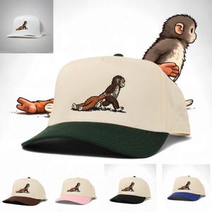 May include: A beige and green baseball cap featuring an embroidered cartoon monkey design. The cap has a curved brim and a snapback closure. Additional caps with brown, pink, black, and blue brims are also shown.