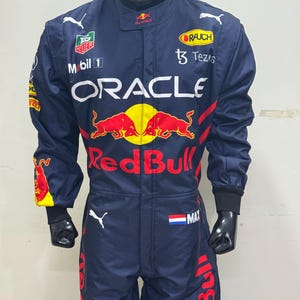 May include: Navy blue racing suit with multiple sponsor logos, including "Oracle" and "Red Bull." The suit features red and yellow accents, a Dutch flag patch, and the name "MAX." A black helmet is also visible.