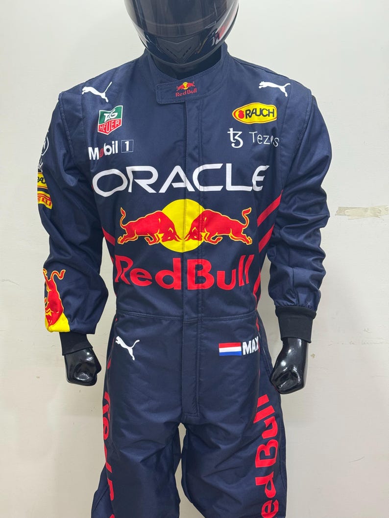 May include: Navy blue racing suit with multiple sponsor logos, including "Oracle" and "Red Bull." The suit features red and yellow accents, a Dutch flag patch, and the name "MAX." A black helmet is also visible.