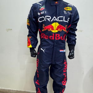 May include: Navy blue racing suit with red and yellow accents. The suit features sponsor logos including "Oracle" and "Red Bull". A black helmet is on top. The suit is displayed on a mannequin.