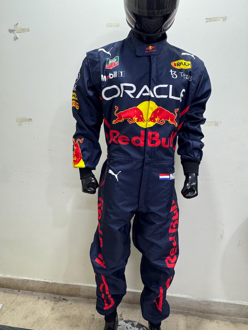 May include: Navy blue racing suit with red and yellow accents. The suit features sponsor logos including "Oracle" and "Red Bull". A black helmet is on top. The suit is displayed on a mannequin.