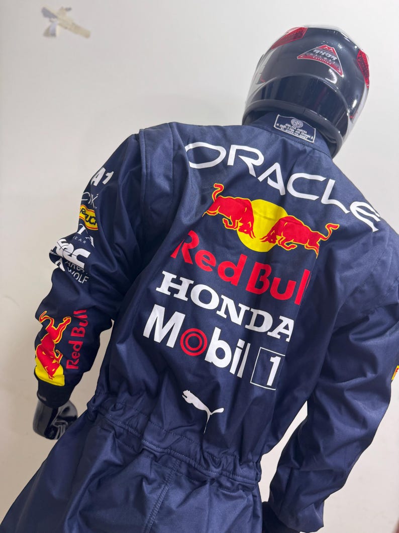May include: Navy blue racing suit with the Red Bull, Honda, and Mobil 1 logos. The suit has a Puma logo and the word "ORACLE" printed on the back. A black helmet is on top of the suit.