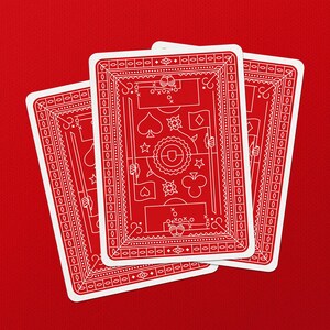 May include: Three playing cards with a red background. The cards have a red face with white decorative elements and suit symbols. The cards are fanned out, showing the backs of the cards.