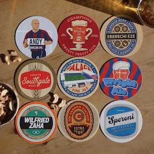 May include: Nine circular beer coasters with football-themed designs. The coasters feature images of players, stadium, and beer-related graphics. Text includes "ANDY JOHNSON IPA", "GARETH SOUTHGATE BEER", "WILFRIED ZAHA", and "EXTRA STOUT".