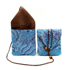 May include: Two small, matching fabric pouches. The pouches have a blue wave pattern with purple accents. One pouch is open, revealing a brown interior. The other pouch is closed with a brown cord and wooden bead closure. A brown cord is attached to each pouch.