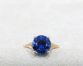 May include: A gold ring featuring a large, round, deep blue gemstone. The gemstone is the focal point, set in a four-prong setting. The band is a simple, elegant design.