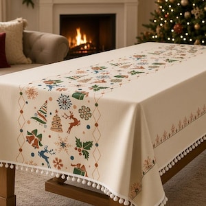 Könnte beinhalten: Eine cremefarbene, rechteckige Tischdecke mit einem zentralen vertikalen Streifen, der mit bunten Weihnachtsmotiven wie Rentieren, Tannenbäumen, Glocken, Schneeflocken und Stechpalmen verziert ist und einen weißen Bommelbesatz hat.