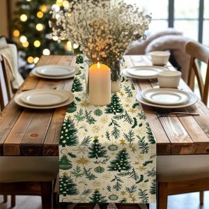 Op de afbeelding: Een feestelijke kersttafelsetting met een crèmekleurige loper met groene kerstbomen, gouden sterren en sneeuwvlokken. Een brandende kaars en witte borden maken de feestelijke decoratie compleet. De tafel is van hout.