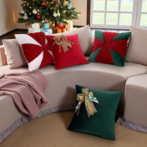 Op de afbeelding: Een verzameling decoratieve kerstkussens in rood, wit en groen fluweel. Sommige kussens hebben strikaccenten. De kussens zijn gerangschikt op een gebogen beige bank, met een kerstboom op de achtergrond.