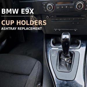 Könnte beinhalten: Ein schwarzer Innenraum eines BMW E9X Fahrzeugs mit einer Mittelkonsole, einem Schalthebel und zwei runden Getränkehaltern, die als Aschenbecherersatz installiert sind. Der Text BMW E9X CUP HOLDERS ASHTRAY REPLACEMENT ist eingeblendet.