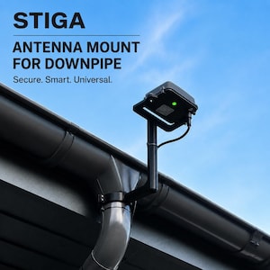 Pode incluir: Um suporte de antena STIGA para tubo de queda fixado a um sistema de calhas cinzento. O dispositivo possui uma caixa retangular preta com uma pequena luz indicadora verde e um cabo preto que se estende da unidade ao suporte.