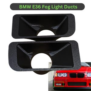 May include: Two black fog light ducts for a BMW E36. The ducts are rectangular with a textured surface and a circular opening. The text "BMW E36 Fog Light Ducts" is at the top. A red BMW car is in the background.